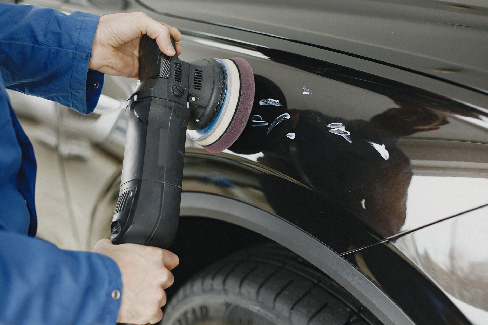 Hands using a polishing machine on a car's surface in a garage setting.
