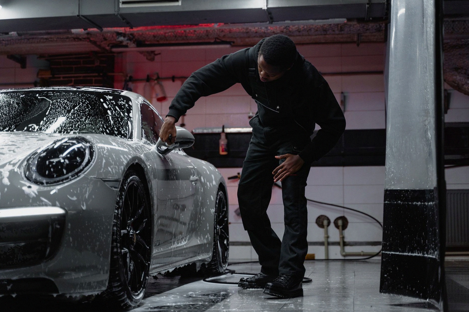 Man washing a luxury car in an indoor garage, emphasizing automotive care.