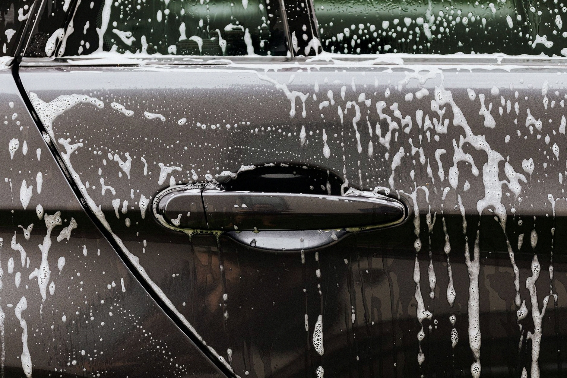 Detailed close-up of soap suds on a black car door during a wash, highlighting automotive care.